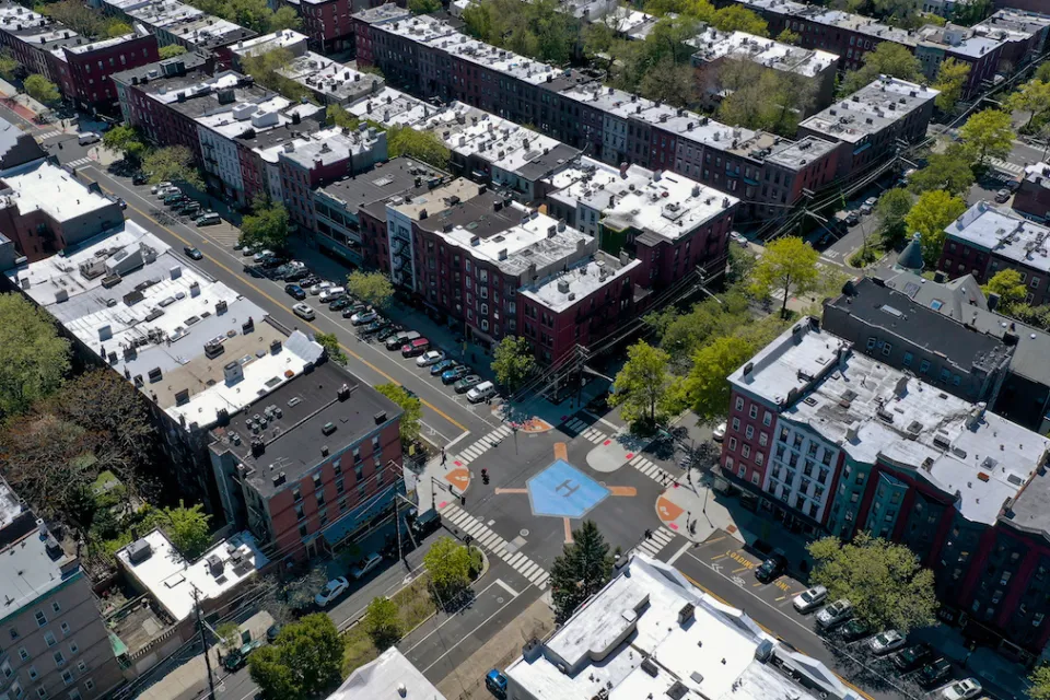 Aerial view of intersection in Hoboken, New Jersey with crosswalks, bulb-outs, and blue home plate painted in middle of intersection, surrounded by mid-rise multistory apartment buildings.